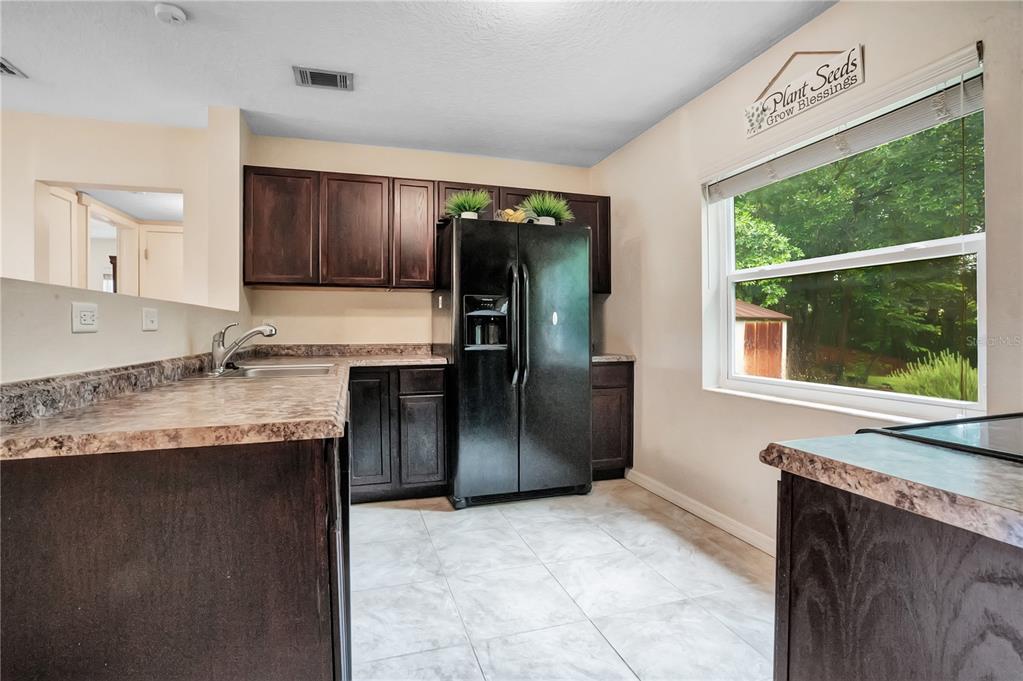 A kitchen features dark wood cabinets, laminate countertops, a black refrigerator, and tile flooring — 4901 BRISTOL COURT, ORLANDO, FL
