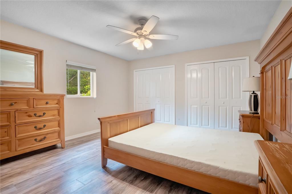 A bedroom features light wood furniture, a ceiling fan, white closet doors, and wood-look flooring — 4901 BRISTOL COURT, ORLANDO, FL