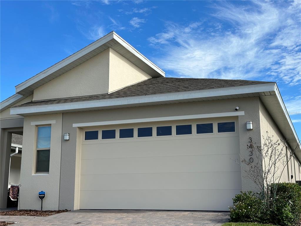 A beige house exterior features a two-car garage with windows and a paved driveway — 3430 SAGEBRUSH STREET, HARMONY, FL