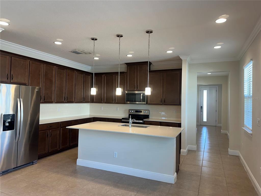 A kitchen features dark wood cabinets, stainless steel appliances, a central island, and tile flooring — 3430 SAGEBRUSH STREET, HARMONY, FL