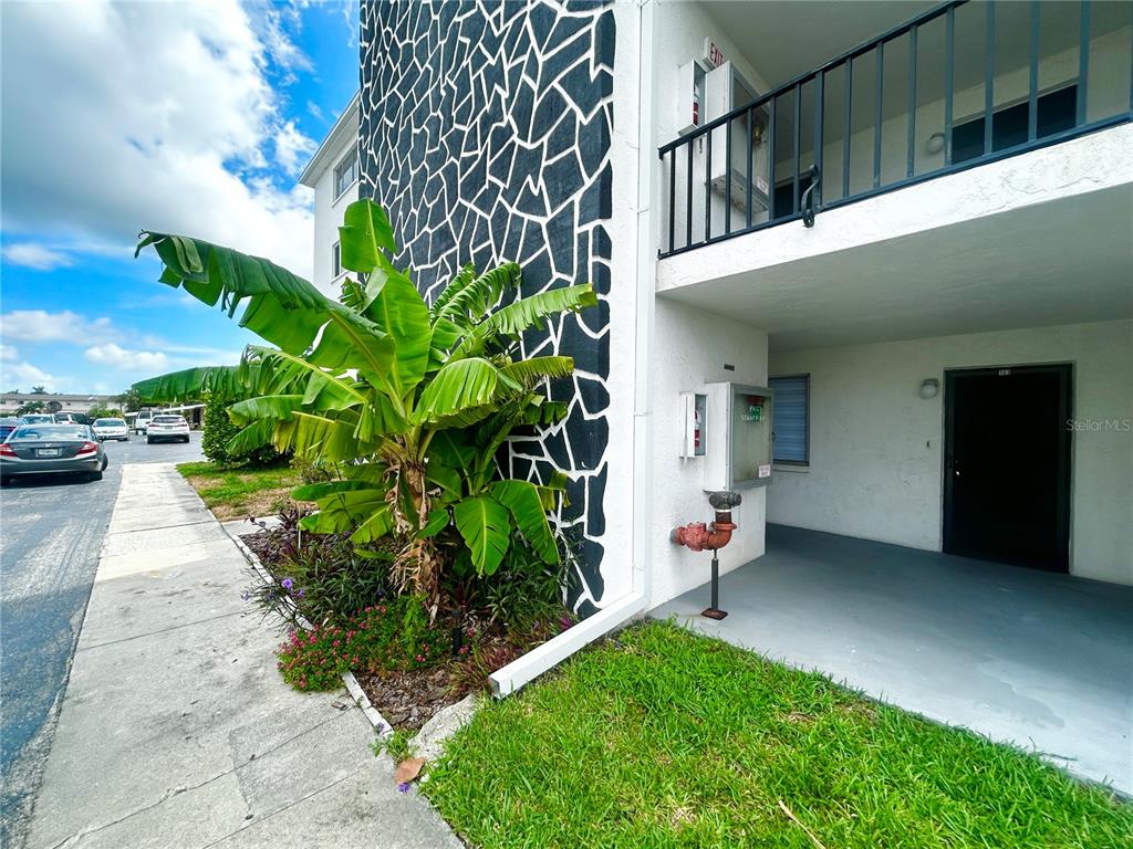Exterior view of a building with a stone-patterned wall, a banana plant, and a balcony — 4906 VICTORIA DRIVE UNIT 103, CAPE CORAL, FL