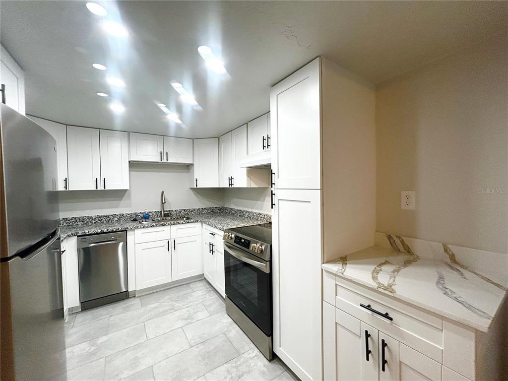 A kitchen features white cabinets, granite countertops, stainless steel appliances, and light-colored tile flooring — 4906 VICTORIA DRIVE UNIT 103, CAPE CORAL, FL