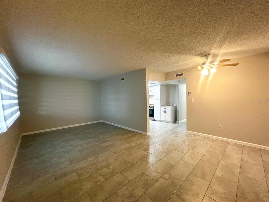 An open-concept living area features light-colored tile flooring, neutral walls, and a ceiling fan — 4906 VICTORIA DRIVE UNIT 103, CAPE CORAL, FL