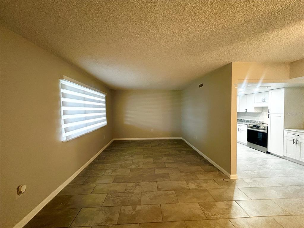 A living area with tile flooring and a window with blinds leads into a kitchen — 4906 VICTORIA DRIVE UNIT 103, CAPE CORAL, FL
