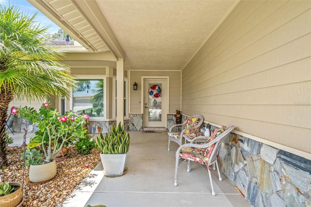 A covered front porch features stone accents, two wicker chairs, and several potted plants — 2485 BROOKLAWN STREET, SPRING HILL, FL