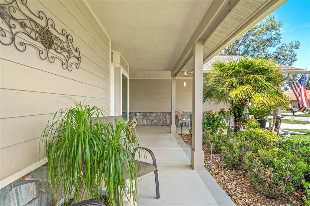 A covered front porch features a concrete floor, stone accents, and a potted palm plant — 2485 BROOKLAWN STREET, SPRING HILL, FL
