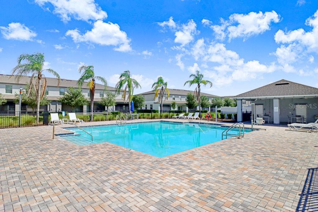 A rectangular swimming pool with a brick paver deck and palm trees under a blue sky — 9536 PEMBROOKE PINES DRIVE, SUN CITY CENTER, FL