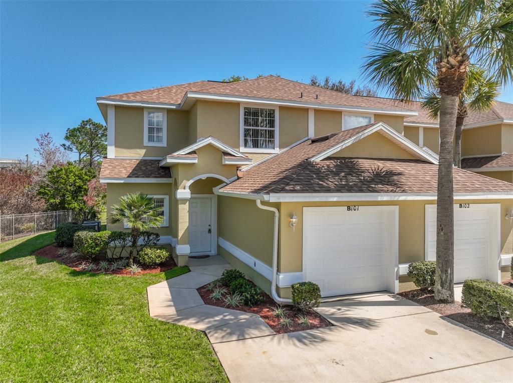 A two-story tan townhouse with a white garage door and a palm tree in front — 2001 PALM DRIVE UNIT B101, FLAGLER BEACH, FL