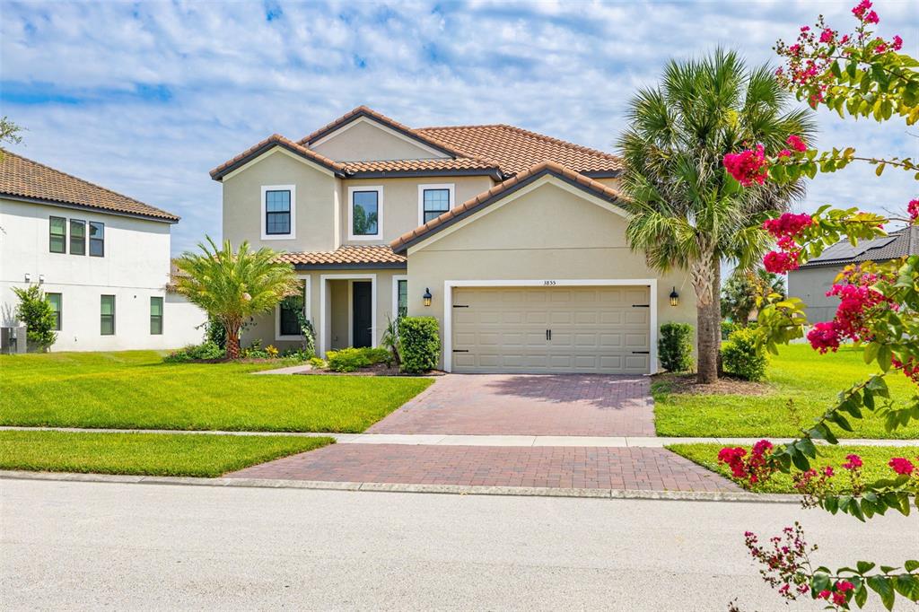 A two-story suburban house with a tan stucco exterior, tile roof, and brick paver driveway — 3855 BOWFIN TRAIL, KISSIMMEE, FL