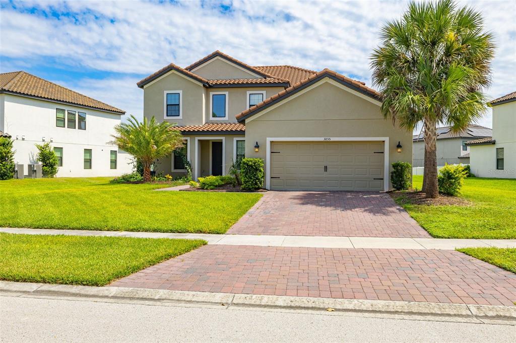 A two-story suburban house with a tan stucco exterior, tile roof, and brick paver driveway — 3855 BOWFIN TRAIL, KISSIMMEE, FL