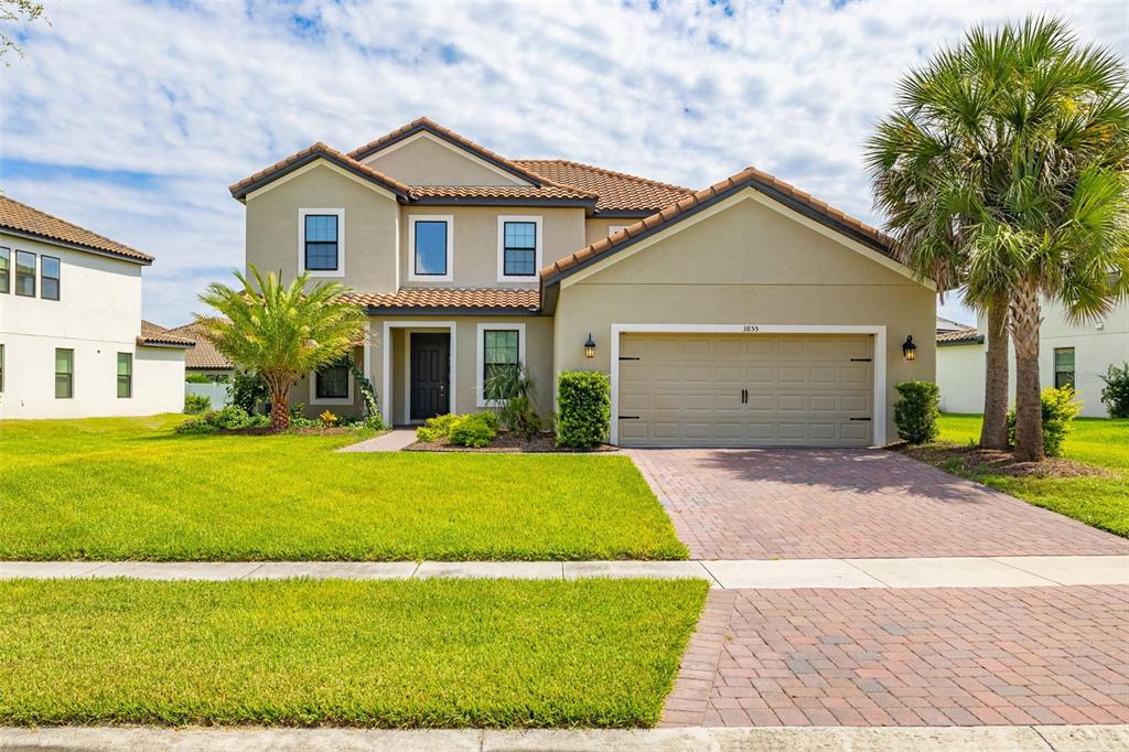 A two-story suburban house features a tan stucco exterior, a tiled roof, and a paved driveway — 3855 BOWFIN TRAIL, KISSIMMEE, FL