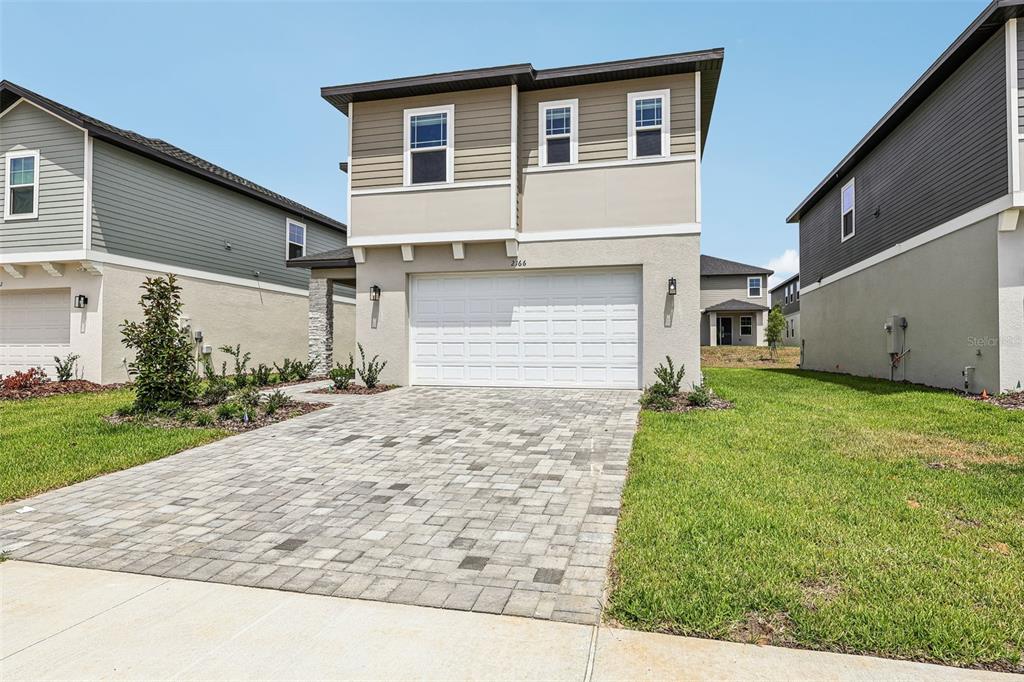 A two-story suburban house with a paved driveway, a two-car garage, and tan siding — 2166 WILDBERRY WAY, MINNEOLA, FL
