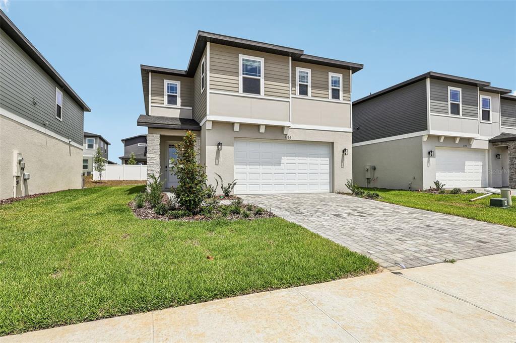 A two-story suburban house with a beige stucco and siding exterior and a paved driveway — 2166 WILDBERRY WAY, MINNEOLA, FL