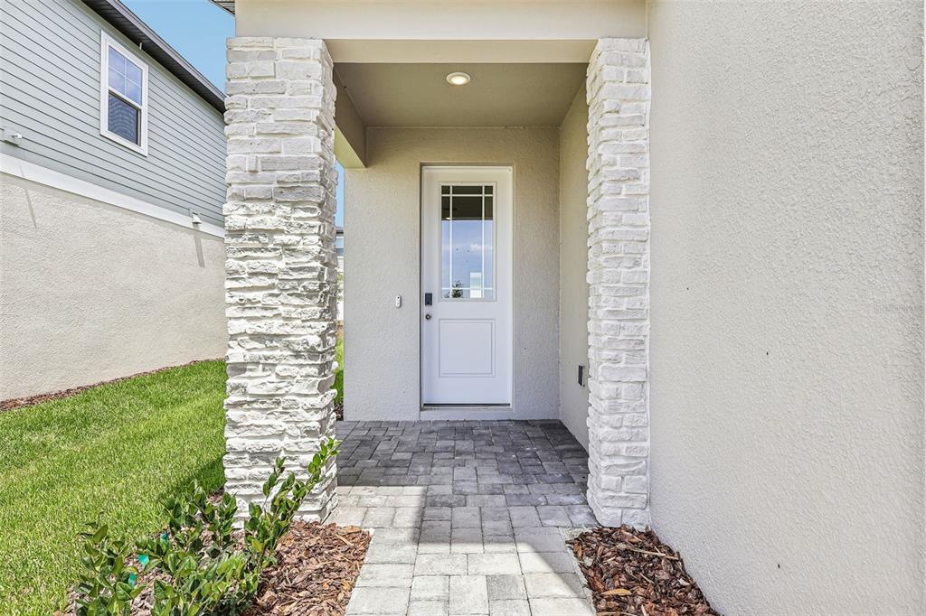 A white front door is framed by two stone columns on a paved entryway porch — 2166 WILDBERRY WAY, MINNEOLA, FL