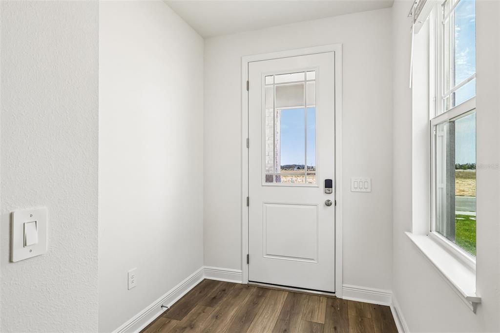 A bright entryway features white walls, wood-look flooring, a glass-paneled door, and a large window — 2166 WILDBERRY WAY, MINNEOLA, FL