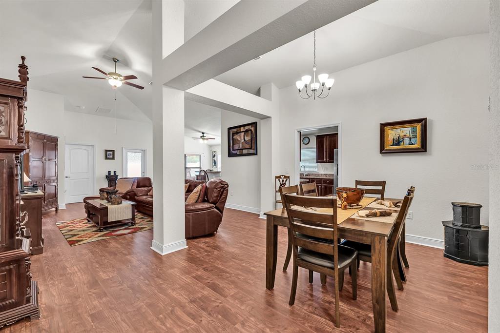 A dining area and living room with wood-look flooring, vaulted ceilings, and neutral walls — 12250 LEGACY BRIGHT STREET, RIVERVIEW, FL