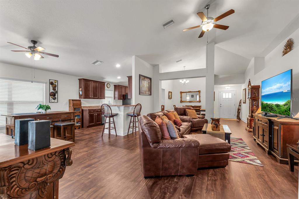 An open-concept living room and kitchen featuring brown leather furniture, wood flooring, and a television — 12250 LEGACY BRIGHT STREET, RIVERVIEW, FL
