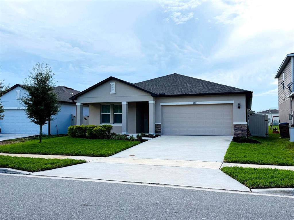 A single-story suburban house features a two-car garage, a concrete driveway, and a small lawn — 1306 AXEL GRAESON AVENUE, KISSIMMEE, FL