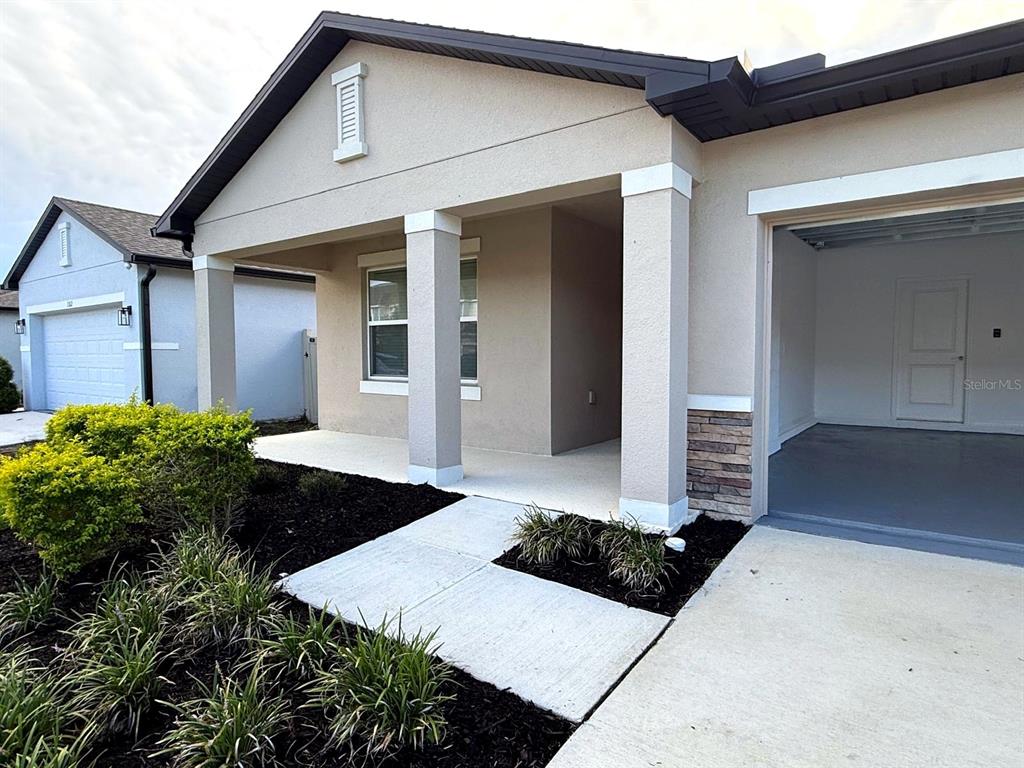 A beige house exterior features a covered front porch, stone accents, and an open garage — 1306 AXEL GRAESON AVENUE, KISSIMMEE, FL