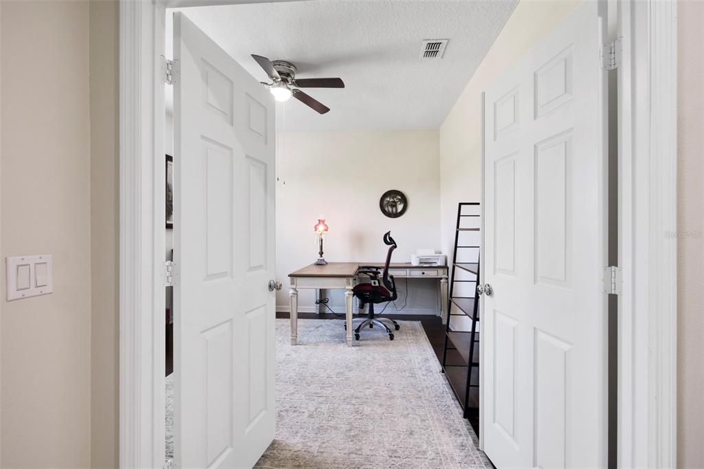A home office features a desk, chair, area rug, and ceiling fan viewed through double doors — 21315 SORRAIA COVE, MOUNT DORA, FL