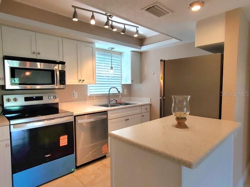 A kitchen features white cabinets, stainless steel appliances, a light countertop, and a track light — 1080 BAL HARBOR BOULEVARD UNIT 10A, PUNTA GORDA, FL
