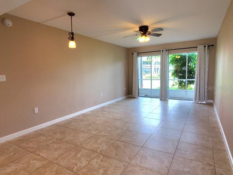 An empty room features beige walls, tile flooring, a ceiling fan, and sliding glass doors — 1080 BAL HARBOR BOULEVARD UNIT 10A, PUNTA GORDA, FL