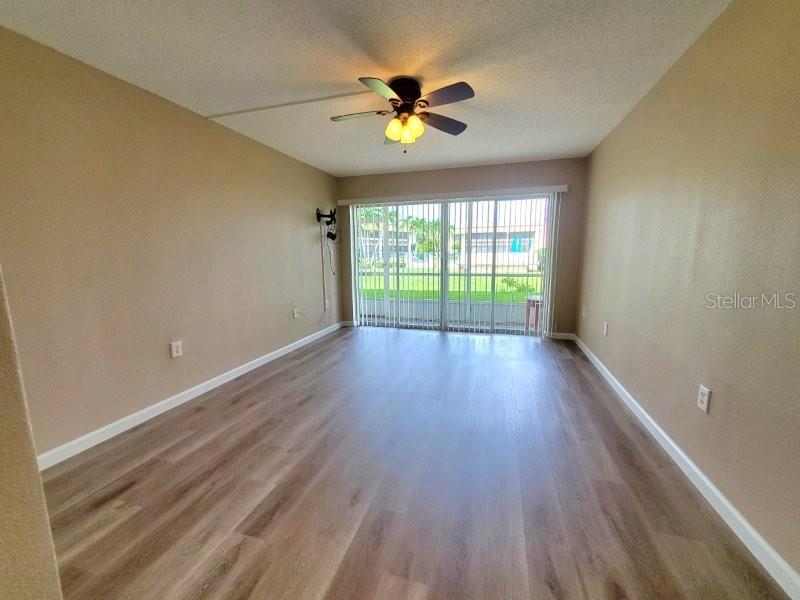 An empty room features light wood-look flooring, beige walls, a ceiling fan, and sliding glass doors — 1080 BAL HARBOR BOULEVARD UNIT 10A, PUNTA GORDA, FL