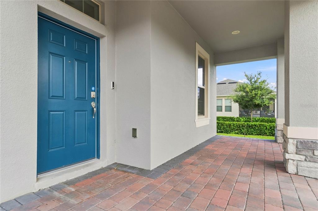 A blue front door opens onto a covered porch with red brick pavers and stone accents — 12728 CHARMED DRIVE, WINTER GARDEN, FL