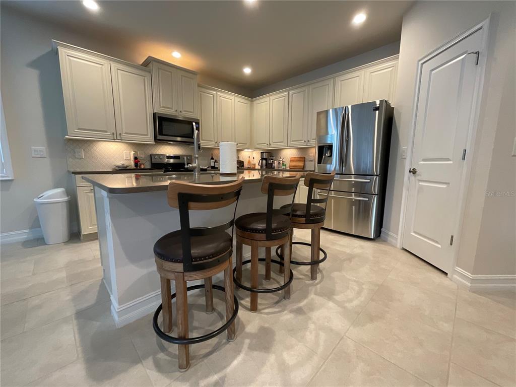 A kitchen features light-colored cabinetry, stainless steel appliances, a center island, and three bar stools — 4428 CONCHFISH LANE, OSPREY, FL