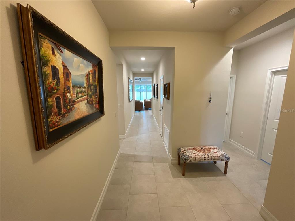 A tiled hallway leads past a framed painting and a bench toward a sunlit room — 4428 CONCHFISH LANE, OSPREY, FL