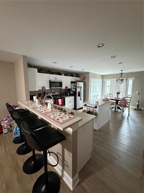 A kitchen features white cabinets, stainless steel appliances, a breakfast bar with stools, and wood-look flooring — 350 S 8TH AVENUE, BARTOW, FL