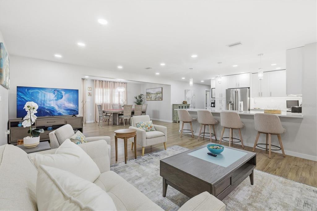 An open-concept living room, dining area, and kitchen feature light wood flooring and neutral furniture — 5247 CARMILFRA DRIVE, SARASOTA, FL