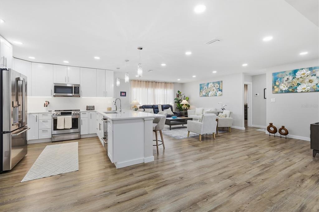 An open-concept kitchen and living area features white cabinetry, a central island, and wood-look flooring — 5247 CARMILFRA DRIVE, SARASOTA, FL