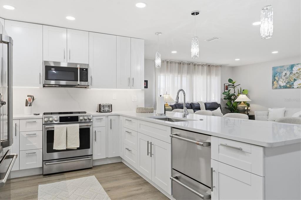 A modern white kitchen features stainless steel appliances, quartz countertops, and an island with seating — 5247 CARMILFRA DRIVE, SARASOTA, FL