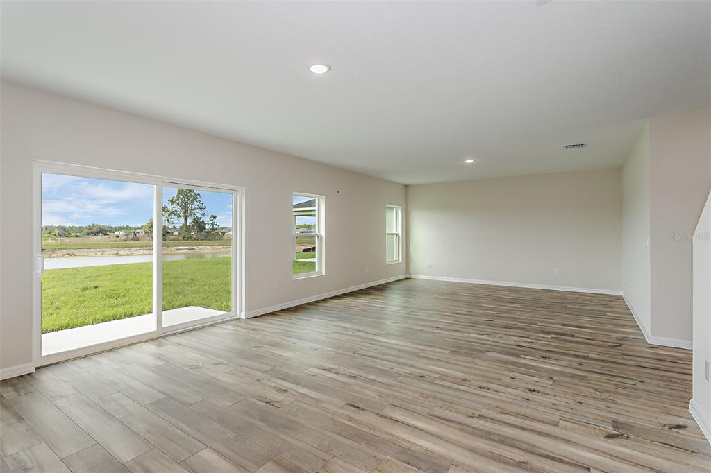 An empty living room features wood-look flooring, recessed lighting, and a sliding glass door to outdoors — 36715 THORNHEDGE DRIVE, ZEPHYRHILLS, FL