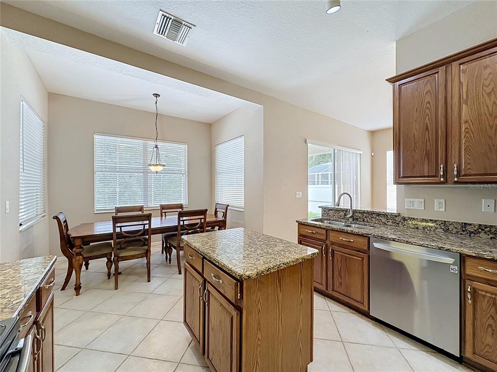 A kitchen with wooden cabinets, granite countertops, a center island, and an adjacent dining area — 468 PINEWOOD DR, DAVENPORT, FL
