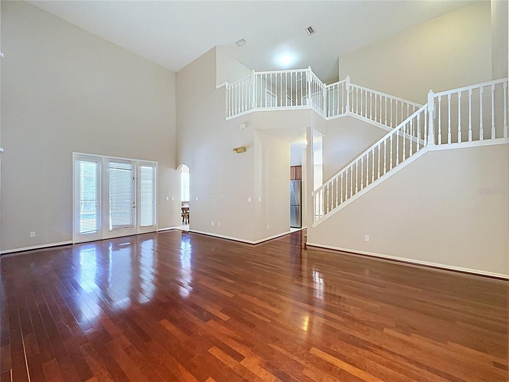 An empty living room features high ceilings, hardwood floors, and a staircase with white railings — 468 PINEWOOD DR, DAVENPORT, FL