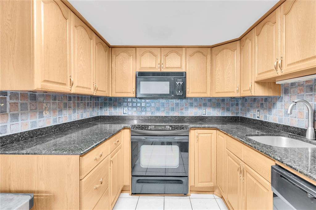 A kitchen with light wood cabinets, dark granite countertops, a tiled backsplash, and black appliances — 1 KEY CAPRI UNIT 303E, TREASURE ISLAND, FL