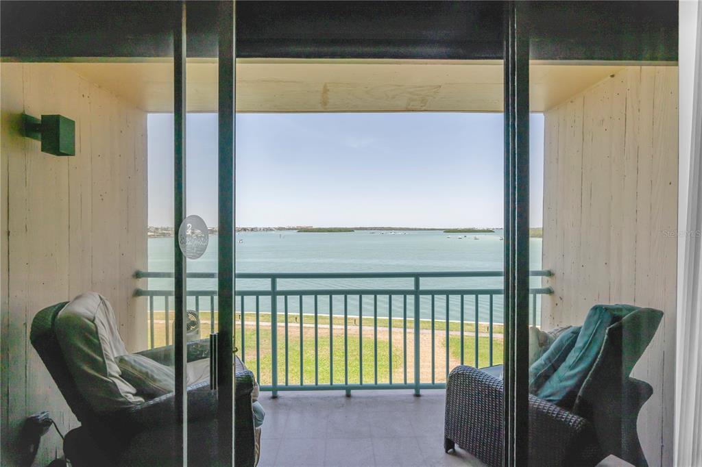 A balcony with two chairs overlooks a body of water and a grassy lawn — 1 KEY CAPRI UNIT 303E, TREASURE ISLAND, FL