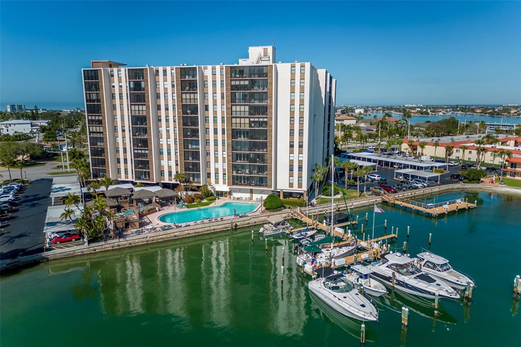 A tall apartment building stands beside a marina filled with boats docked at wooden piers — 10355 PARADISE BOULEVARD UNIT 213, TREASURE ISLAND, FL