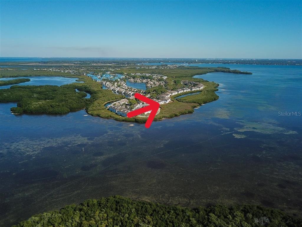 An aerial view shows multi-story apartment buildings with gray siding and tiled roofs near water — 1323 PERICO POINT CIRCLE UNIT 107, BRADENTON, FL