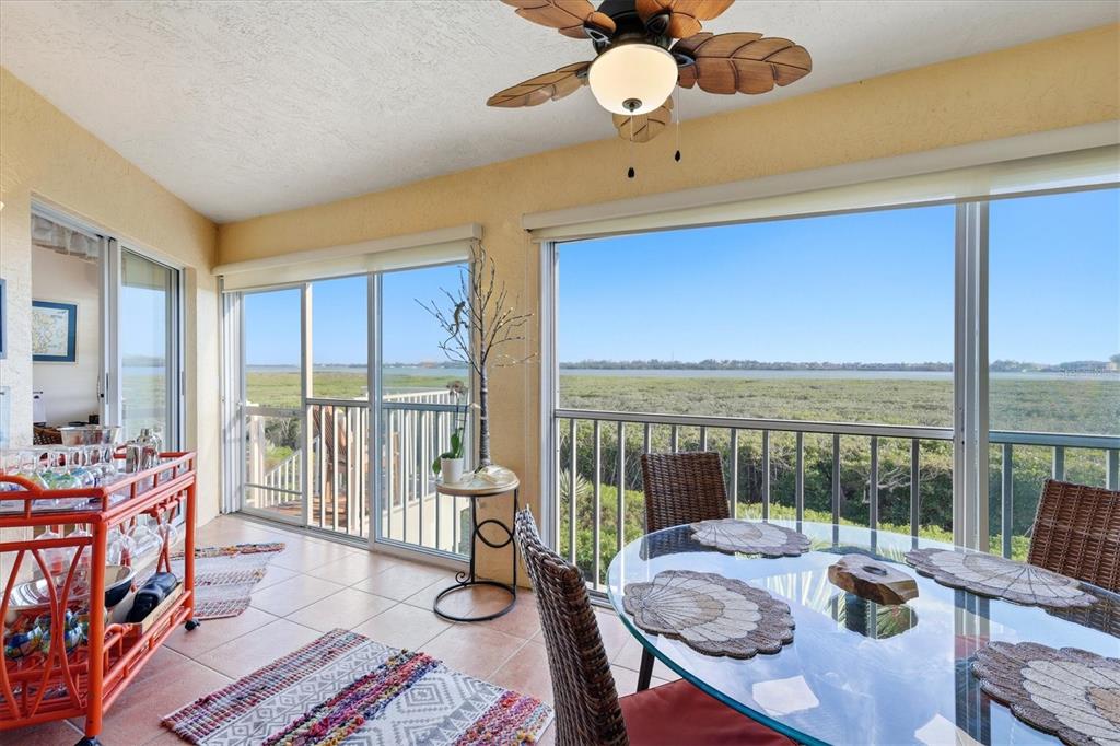 A sunroom features a glass dining table, a bar cart, and sliding doors overlooking wetlands — 1323 PERICO POINT CIRCLE UNIT 107, BRADENTON, FL