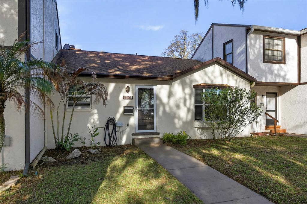 A single-story townhouse with a white stucco exterior, a brown shingled roof, and a walkway — 2207 KARL STREET UNIT B, LEESBURG, FL