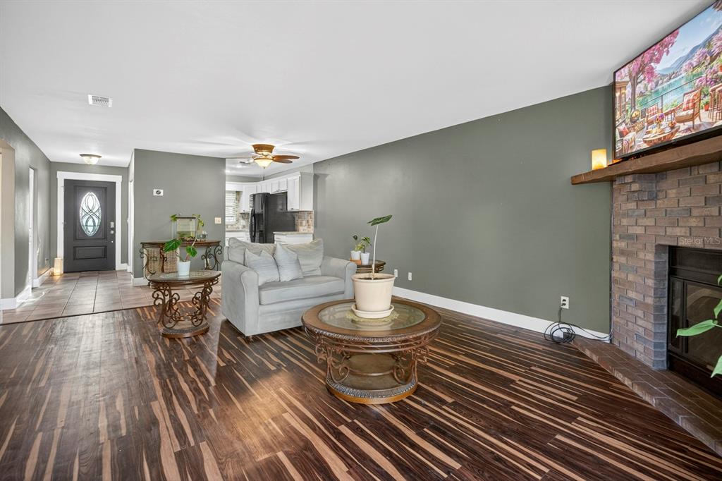 A living room with dark wood-look flooring, a brick fireplace, and a gray accent wall — 2207 KARL STREET UNIT B, LEESBURG, FL