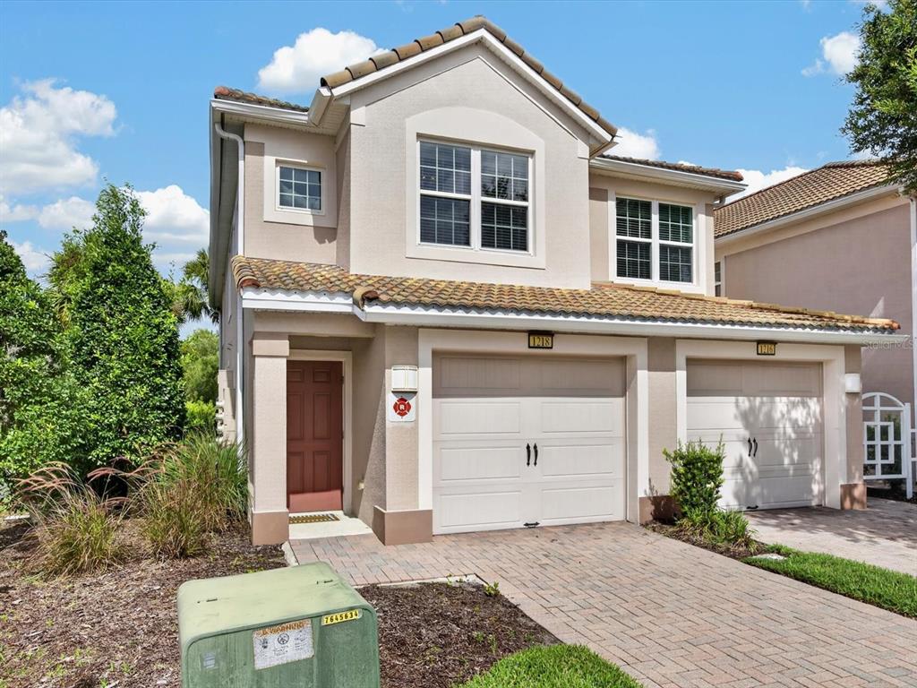 A two-story beige house with a brick driveway, two garage doors, and a brown front door — 1218 BELLA CARA COURT, DAVENPORT, FL