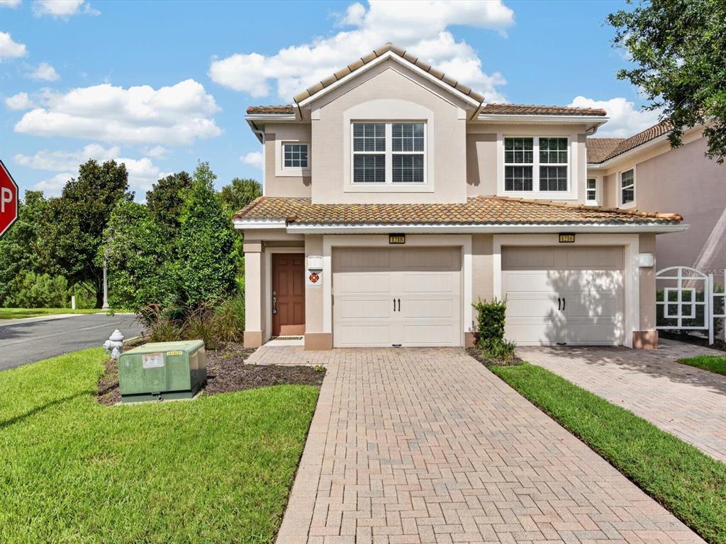 A two-story townhouse with a beige stucco exterior, two garage doors, and a paved driveway — 1218 BELLA CARA COURT, DAVENPORT, FL