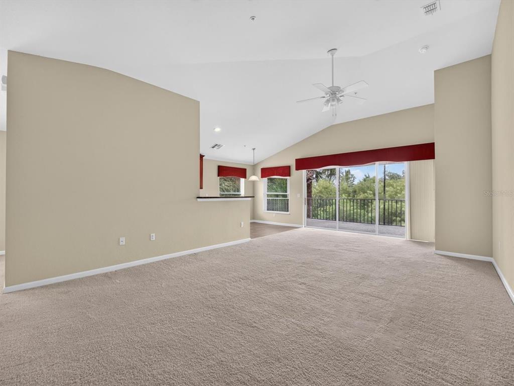 A spacious living room features beige carpet, vaulted ceilings, a ceiling fan, and sliding glass doors — 1218 BELLA CARA COURT, DAVENPORT, FL