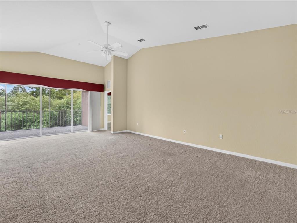 A spacious living room with beige carpet, vaulted ceilings, and a sliding glass door balcony — 1218 BELLA CARA COURT, DAVENPORT, FL