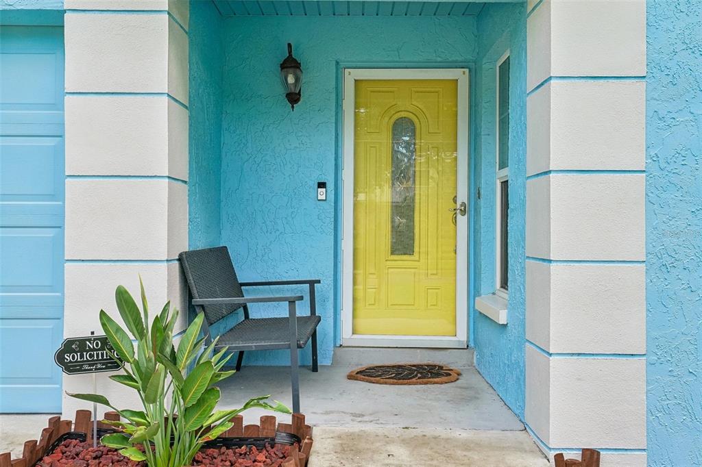 A bright blue exterior wall features a yellow front door and a dark patio chair — 4717 W PRESCOTT STREET, TAMPA, FL