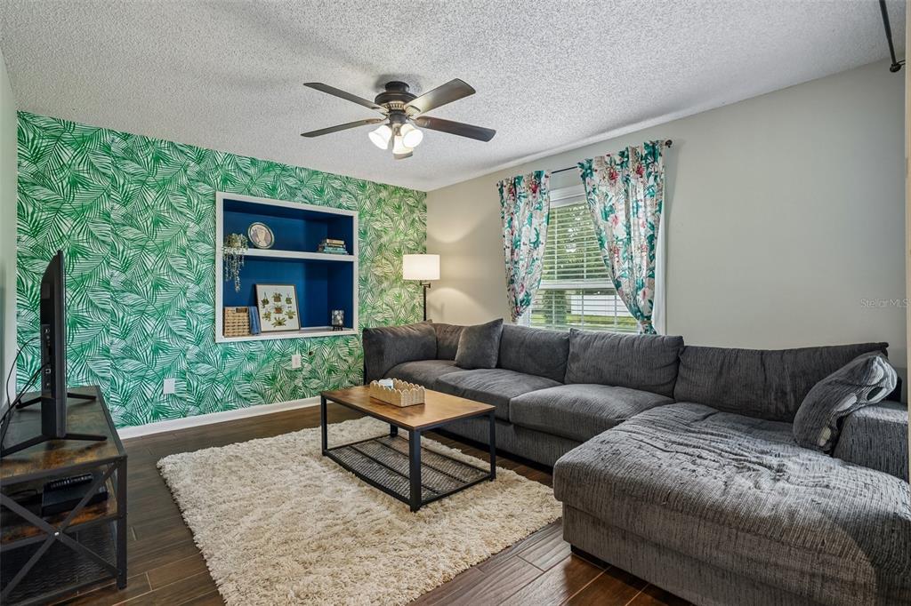 A living room features a palm-leaf wallpaper accent wall, a blue built-in shelf, and sectional sofa — 4717 W PRESCOTT STREET, TAMPA, FL